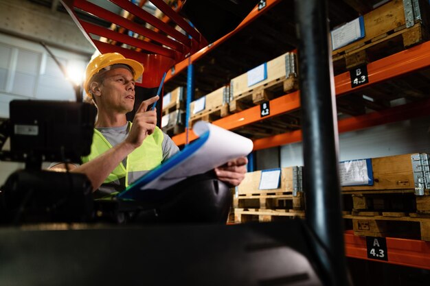 Peinzende heftruckchauffeur die de voorraad pakketten op planken in een magazijn onderzoekt