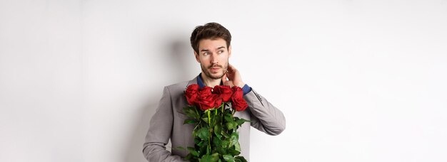 Peinzende jonge man in pak met boeket bloemen wachtend op een datum op Valentijnsdag die overeind staat