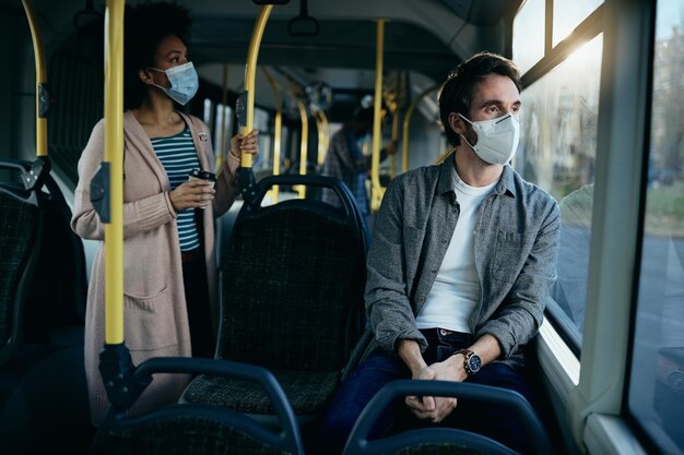 Peinzende man met gezichtsmasker pendelen met de bus en kijken door het raam