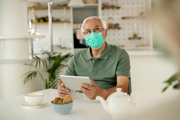 Peinzende senior man die thuis digitale tablet gebruikt tijdens een pandemie van het coronavirus