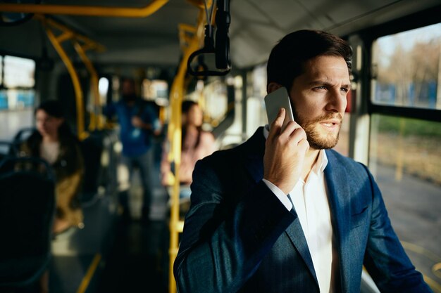 Peinzende zakenman die aan de telefoon praat tijdens het woon-werkverkeer met de bus