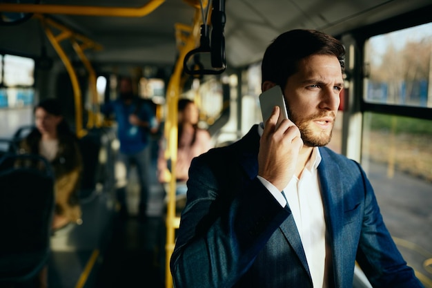 Peinzende zakenman die aan de telefoon praat tijdens het woon-werkverkeer met de bus