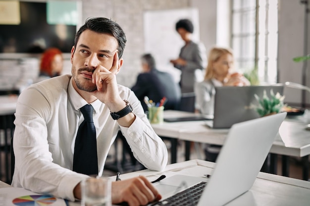 Peinzende zakenman die aan een bureau op kantoor zit en aan nieuwe ideeën denkt Er zijn mensen op de achtergrond