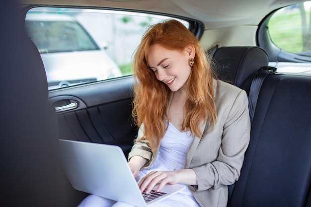 Peinzende zakenvrouw met laptop op de achterbank van de auto Jonge vrouw die een laptop in een auto gebruikt