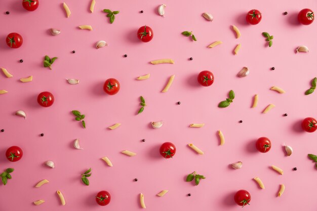 Penne macaron en verschillende ingrediënten op roze achtergrond. Pasta, tomaten, knoflook, peperkorrels op roze achtergrond. Bron van koolhydraten in uw uitgebalanceerde voeding. Tops voor traditionele Italiaanse gerechten