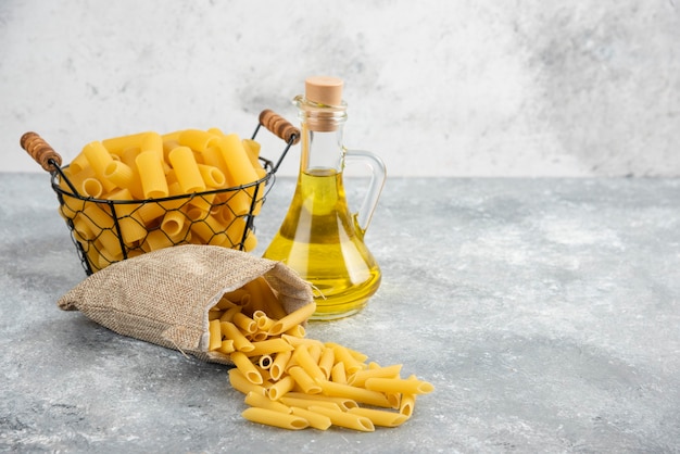 Penne pasta in een metalen container met olijfolie op grijs marmeren tafel.