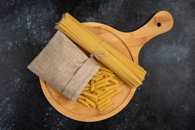 Penne pasta in een rustieke mand met spaghetties op een houten schotel.