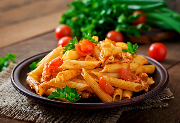 Penne pasta in tomatensaus met kip en tomaten op een houten tafel