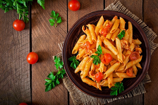 Penne pasta in tomatensaus met kip en tomaten op een houten tafel