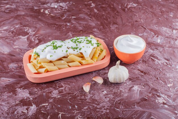 Penne pasta met mayonaise en teentjes knoflook op een lichte tafel.