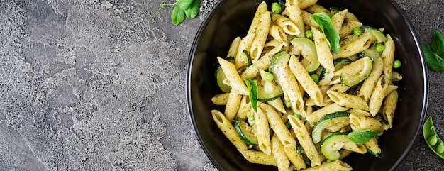 Penne pasta met pestosaus, courgette, doperwtjes en basilicum. Italiaans eten. Bovenaanzicht. Plat liggen.