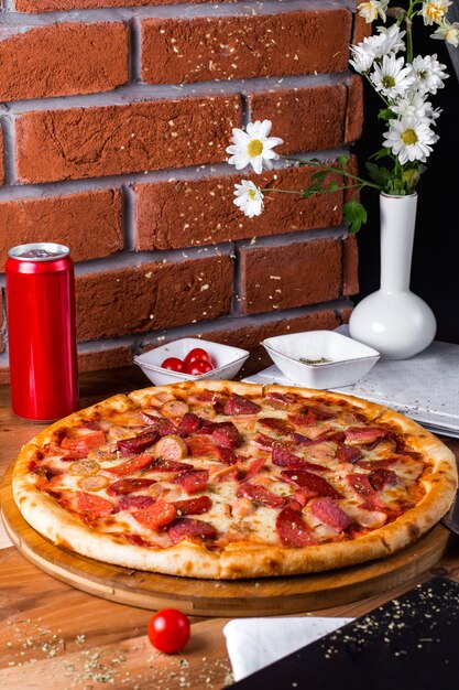 Pepperoni pizza met tomaten en frisdrankblikje op tafel