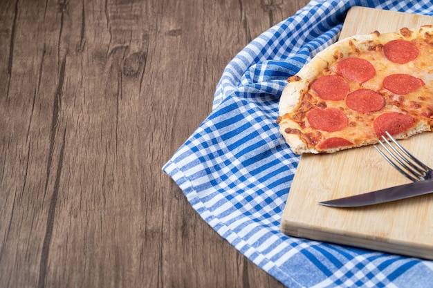 Pepperoni-pizzaplakken op een houten bord met mes en vork eromheen?