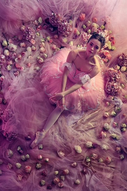 Perfecte uitstraling. bovenaanzicht van mooie jonge vrouw in roze ballet tutu omgeven door bloemen. lentestemming en tederheid in koraallicht. kunst foto. concept van de lente, bloesem en het ontwaken van de natuur.