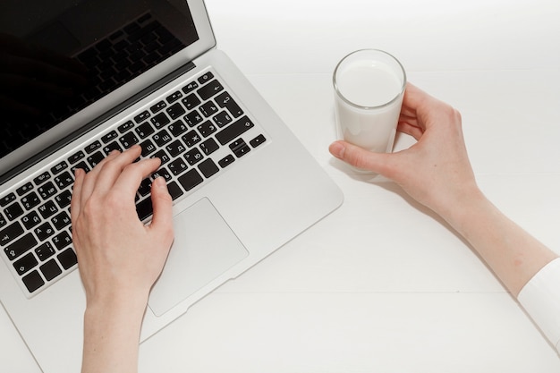 Persoon die aan laptop naast een glas melk werkt