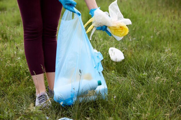 Persoon die bordeauxrode broeken draagt die strooisel van groen gras opneemt en afval in pakketzak zet