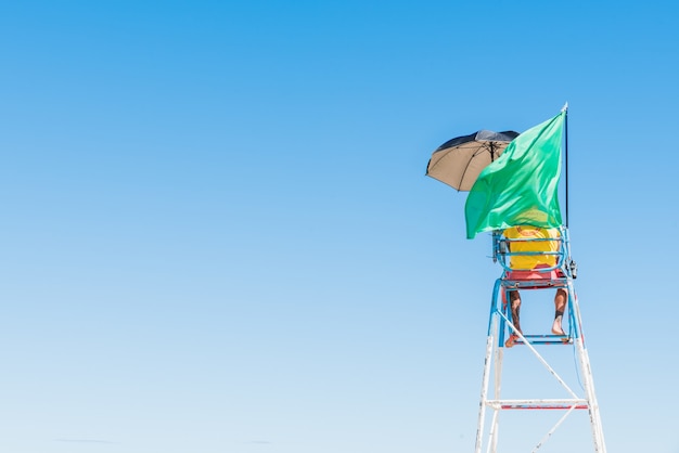 Persoon die op de veiligheidsstoel op het strand staat met een wuivende groene vlag