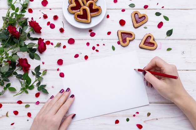 Persoon die op een Witboek met een rood potlood dichtbij hartvormige koekjes met rozenblaadjes trekt