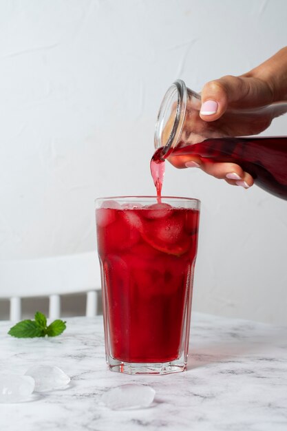 Persoon die verfrissende hibiscus-ijsthee giet in een doorzichtige glazen container