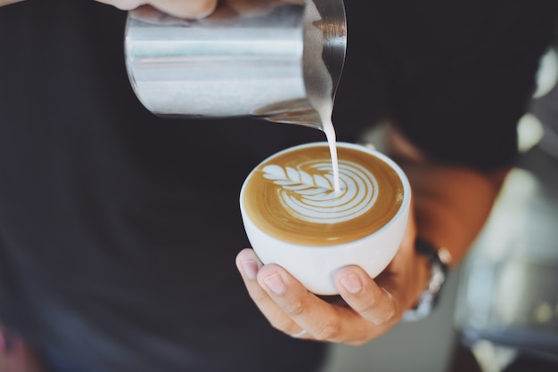 Persoon in dienst van een kopje koffie met een metalen kruik