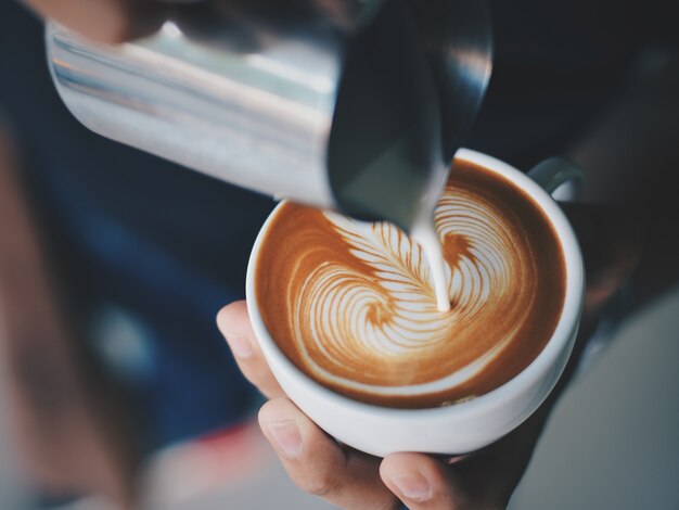 Persoon in dienst van een kopje koffie met een metalen kruik