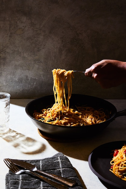 Persoon krijgt wat spaghetti uit een zwarte pot op een witte tafel