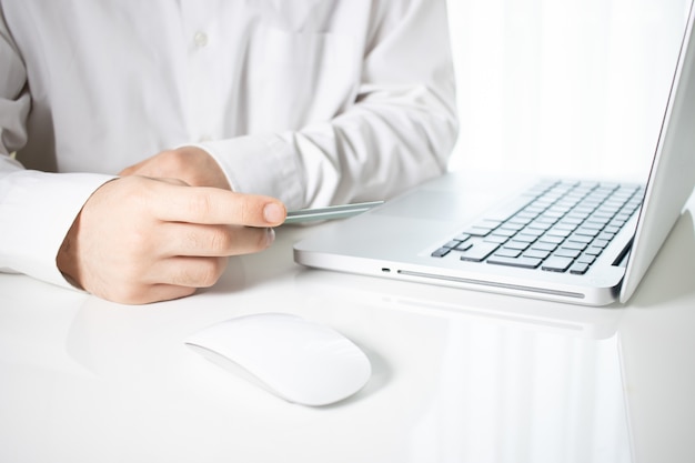 Persoon met een creditcard met een laptop en een computermuis op een witte tafel