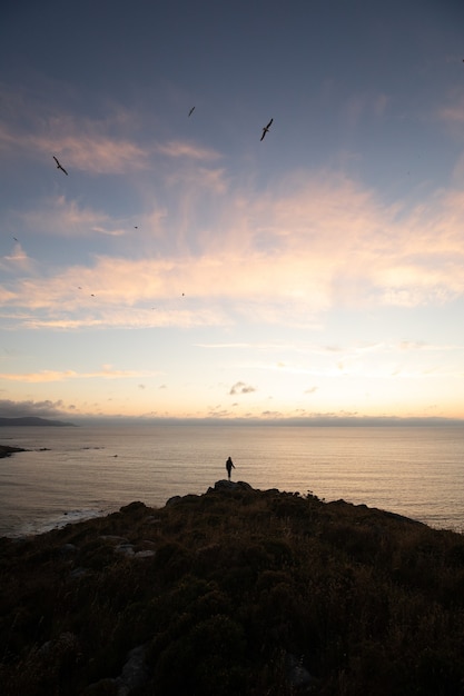 Persoon staande op de top van een heuvel aan zee bij zonsondergang - succes concept