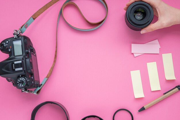 Persoonshand die cameralens met camera en kleverige nota&#39;s houdt; pen over roze achtergrond