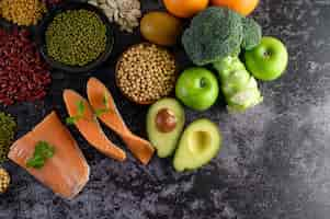 Gratis foto peulvruchten, broccoli, fruit en zalm op een zwarte cementvloer.