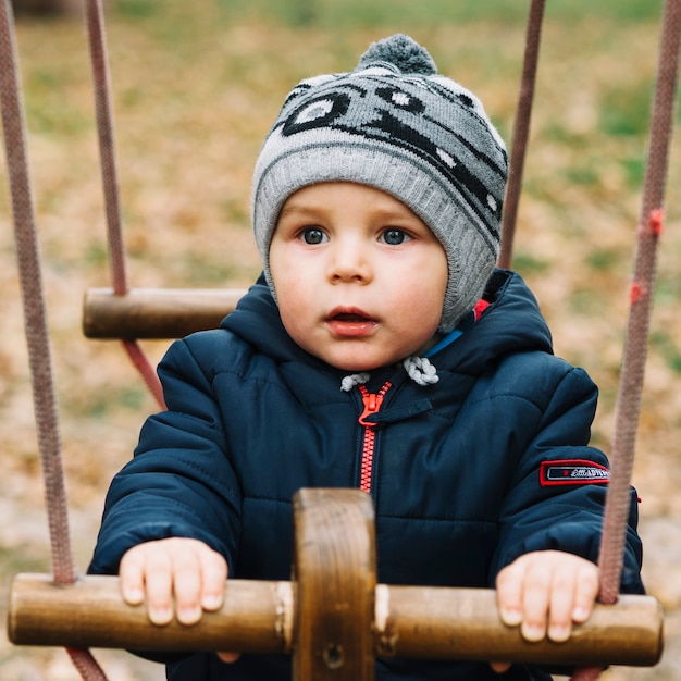 Gratis foto peuterjongen in warme kleren op geschommel