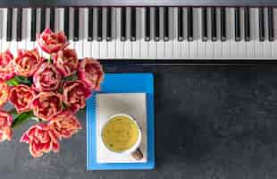 Gratis foto piano bloemen notitieblokken en een kop thee op een donkere achtergrond top view