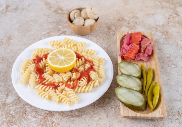 Pickle tray en champignonkom vergezeld van pastaschotel op marmeren oppervlak