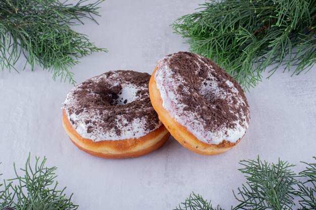 Gratis foto pijnboomtakken rond twee donuts op witte achtergrond.