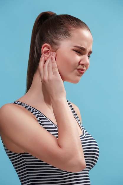 Gratis foto pijnlijk oor de droevige huilende vrouw met hoofdpijn of pijn op trendy blauwe studioachtergrond