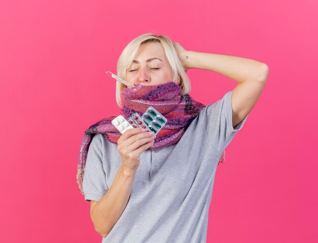 Pijnlijke jonge blonde zieke Slavische vrouw die sjaal draagt legt hand op hoofd achter bedrijfspakken