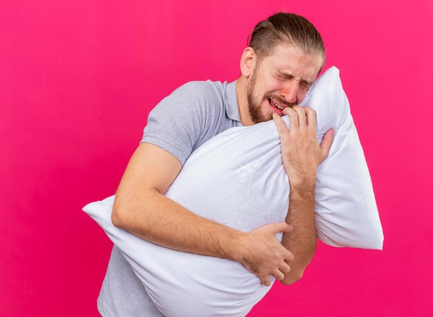 Pijnlijke jonge knappe Slavische zieke man knuffelen kussen met gesloten ogen geïsoleerd op roze muur