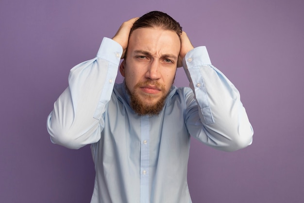 Pijnlijke knappe blonde man houdt hoofd geïsoleerd op paarse muur