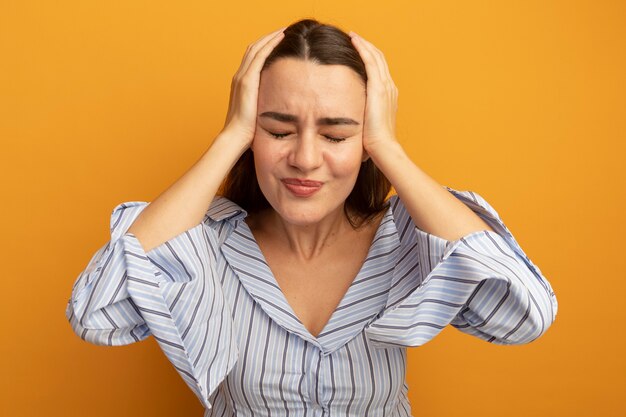 Pijnlijke mooie vrouw houdt hoofd geïsoleerd op oranje muur