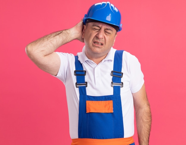 Pijnlijke volwassen blanke bouwer man in uniform legt hand op hoofd geïsoleerd