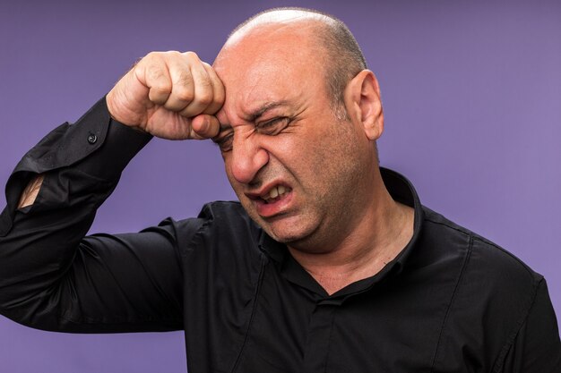 pijnlijke volwassen zieke blanke man zet vuist op voorhoofd geïsoleerd op paarse muur met kopie ruimte