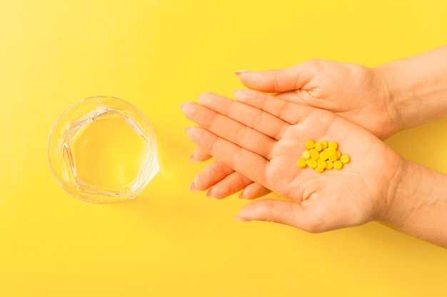 Pillen over de hand van de vrouw met een glas water over de gele achtergrond