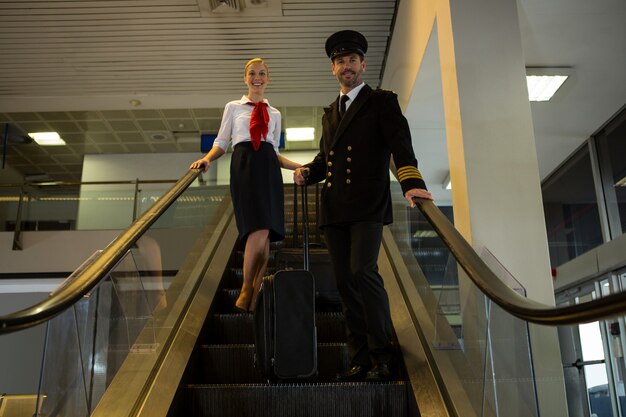 Piloot en stewardess met hun trolleytassen op roltrap