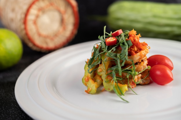 Pittige limoensalade met bittere meloen, laos, chili, tomaten en knoflook in een witte plaat op een zwarte cementvloer.