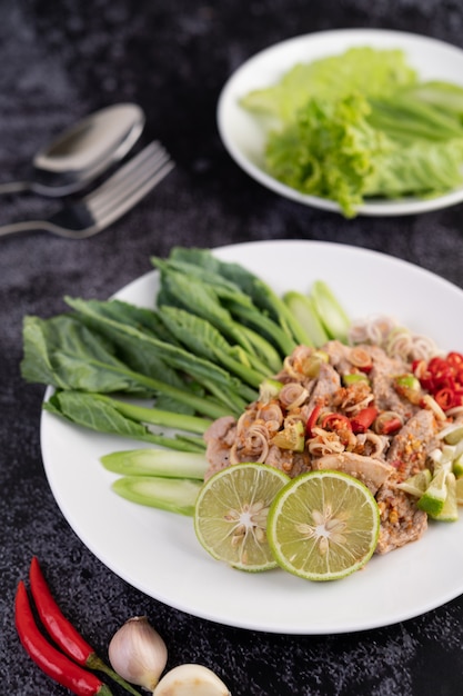 Pittige limoensalade met boerenkool, laos, spaanse peper en knoflook in een witte plaat op een zwarte cementvloer.