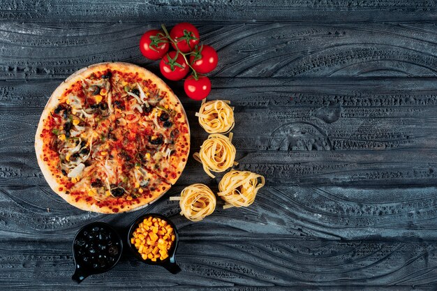 Pizza met spaghetti, tomaten, olijven, maïs bovenaanzicht op een donkerblauwe achtergrond