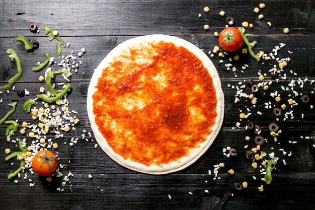 Pizzadeeg met tomatensaus naast kaas hagelslag olijf maïs tomaat paprika