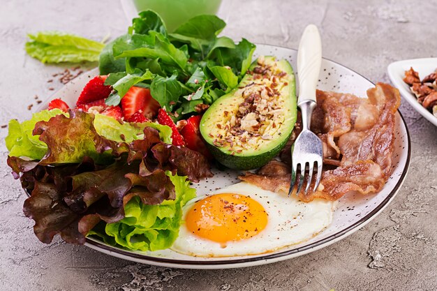 Plaat met een Keto dieetvoeding. Gebakken ei, spek, avocado, rucola en aardbeien. Keto ontbijt.