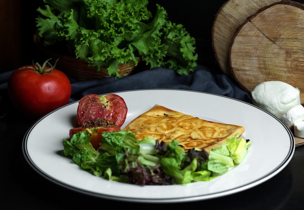 Plaat van crêpe met kaas geserveerd met slasalade en gegrilde tomaat