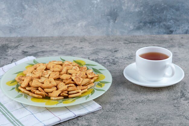 Plaat van gezouten crackers en kop hete thee op marmeren achtergrond.